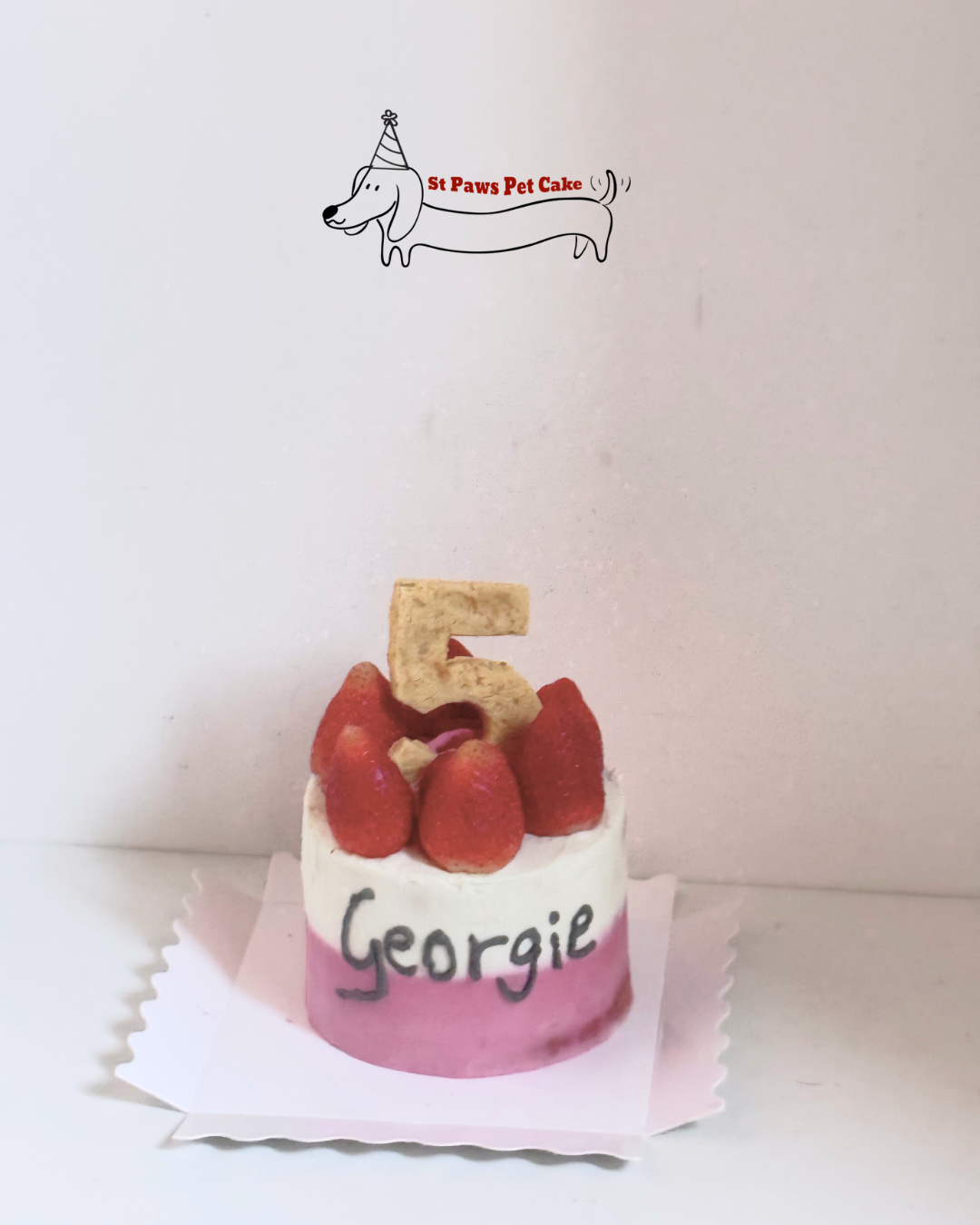 Dog birthday cake with number 5 and strawberries on a white background, branded 'St Paws Pet Cake'. Two toned birthday cake with Turkey Breast fillings with strawberries